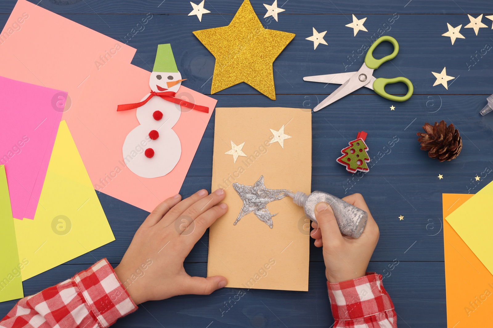 Photo of Little child making Christmas card at blue wooden table, top view