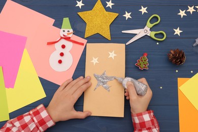 Little child making Christmas card at blue wooden table, top view