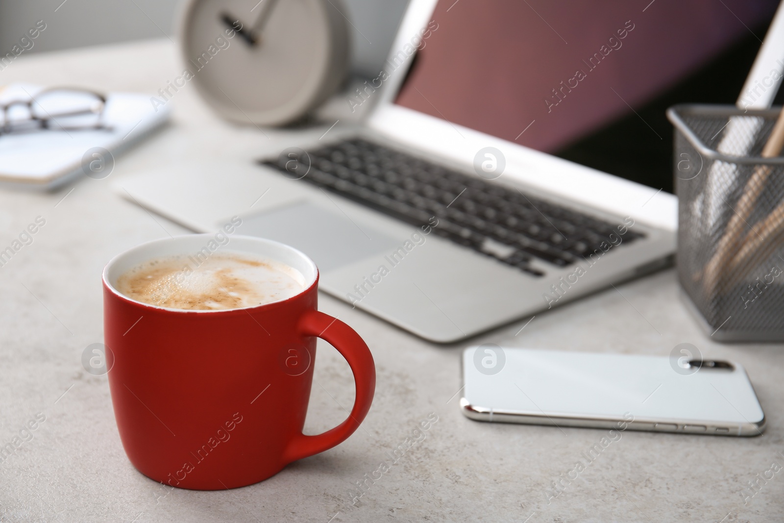 Photo of Red cup with coffee and phone near laptop on office table. Break time