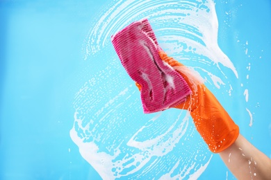 Photo of Woman cleaning glass with rag against color background