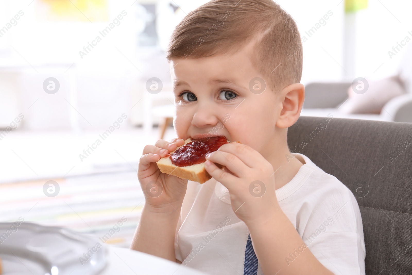 Photo of Cute little boy eating toast with sweet jam at table