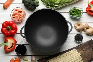 Empty iron wok and raw ingredients on white wooden table, flat lay