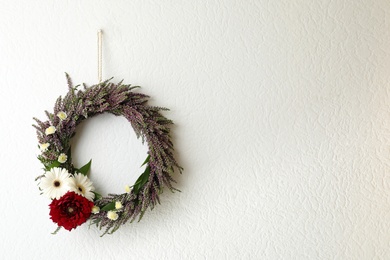 Photo of Beautiful autumnal wreath with heather flowers hanging on white wall. Space for text