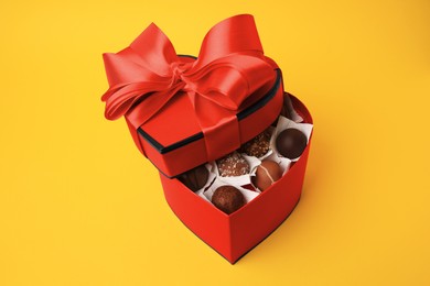 Photo of Heart shaped box with delicious chocolate candies on yellow background