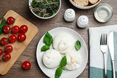 Photo of Delicious burrata cheese with basil served on wooden table, flat lay