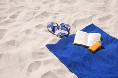 Photo of Soft blue beach towel, flip flops, sunblock and book on sand, space for text