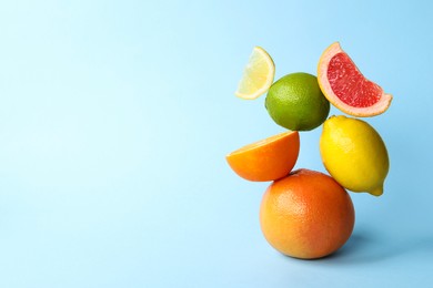 Photo of Fresh ripe citrus fruits on light blue background, space for text