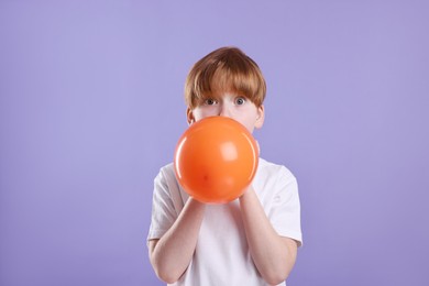 Boy inflating orange balloon on violet background