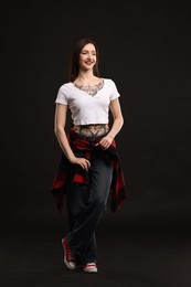 Full length portrait of smiling tattooed woman on black background