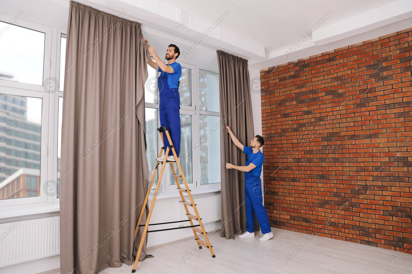 Photo of Workers in uniform hanging window curtain indoors