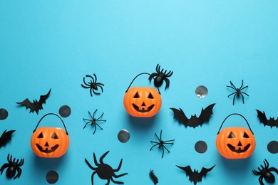 Flat lay composition with plastic pumpkin baskets, paper bats and spiders on light blue background, space for text. Halloween celebration
