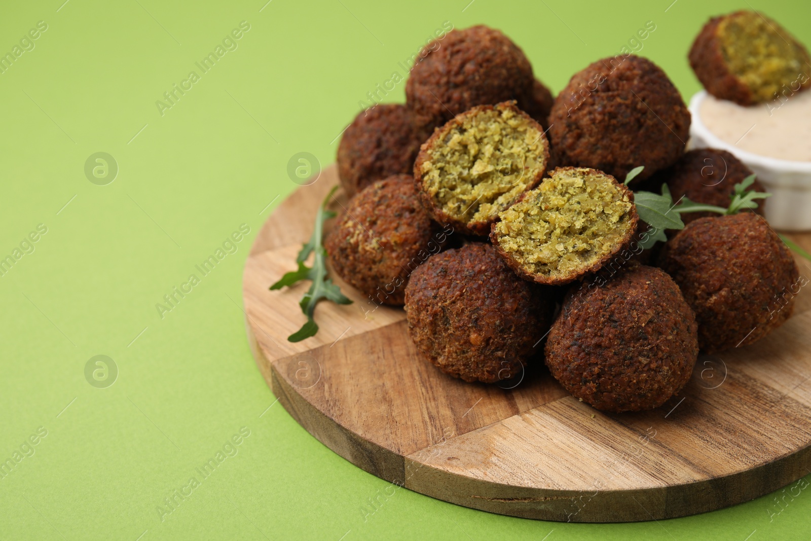 Photo of Delicious falafel balls, arugula and sauce on green background, space for text