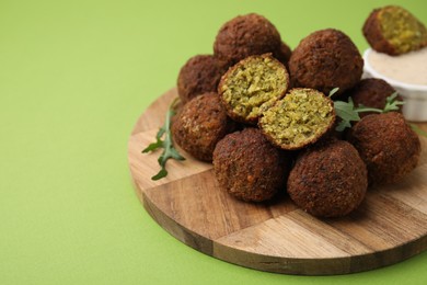 Photo of Delicious falafel balls, arugula and sauce on green background, space for text