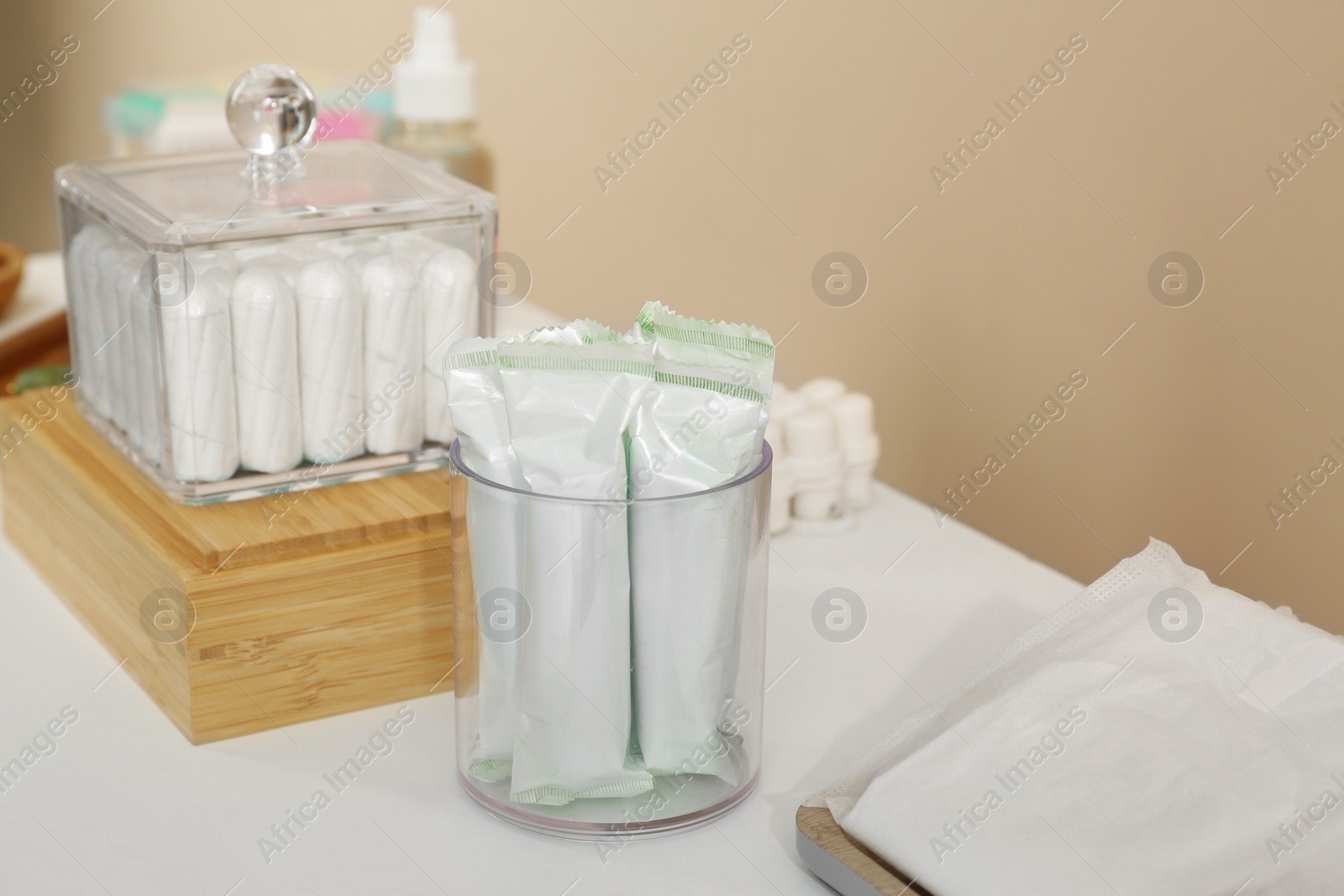 Photo of Holders with many tampons and feminine hygiene products on white table near beige wall. Menstrual hygienic product