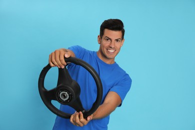 Photo of Happy man with steering wheel on light blue background