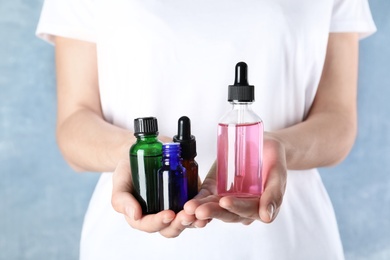 Photo of Woman holding bottles of essential oil on blue background, closeup