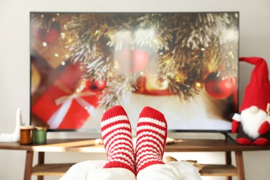 Photo of Woman in cute knitted socks watching TV at home, closeup