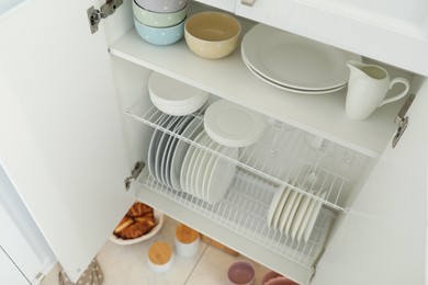 Clean plates, bowls and glasses on shelves in cabinet indoors