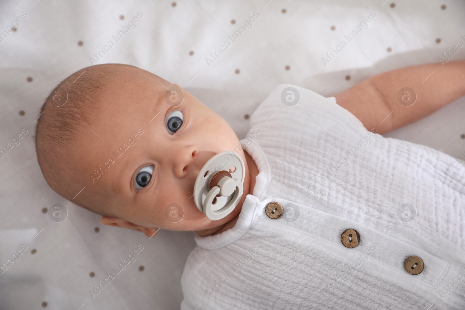 Photo of Cute little baby with pacifier lying on bed, top view