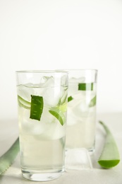 Photo of Fresh aloe drink in glasses and leaves on light table, closeup