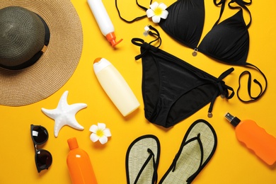 Photo of Flat lay composition with black swimsuit and beach accessories on yellow background