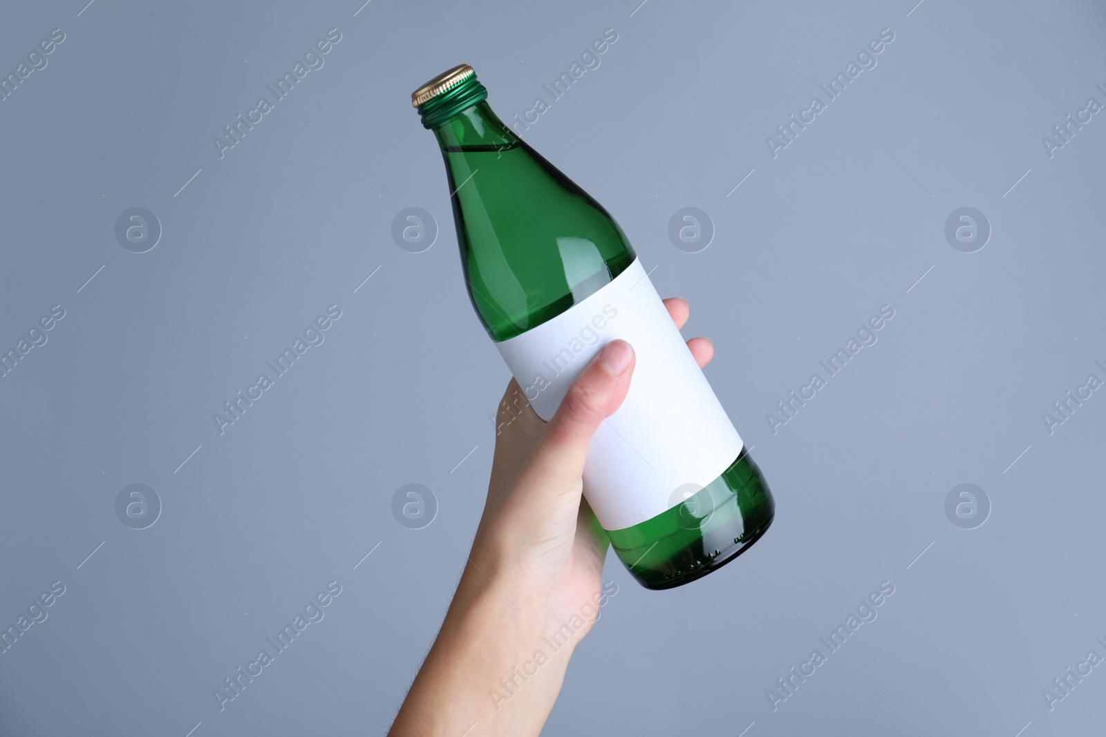 Photo of Woman holding glass bottle with soda water on light grey background, closeup