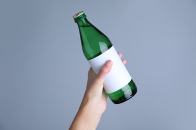 Woman holding glass bottle with soda water on light grey background, closeup