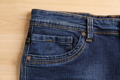 Stylish dark blue jeans on wooden background, closeup of inset pocket