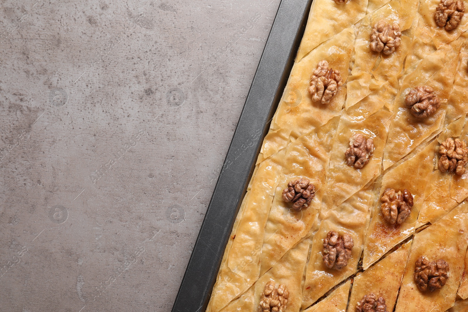 Photo of Delicious baklava with walnuts in baking pan on grey textured table, top view. Space for text