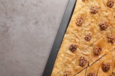 Photo of Delicious baklava with walnuts in baking pan on grey textured table, top view. Space for text