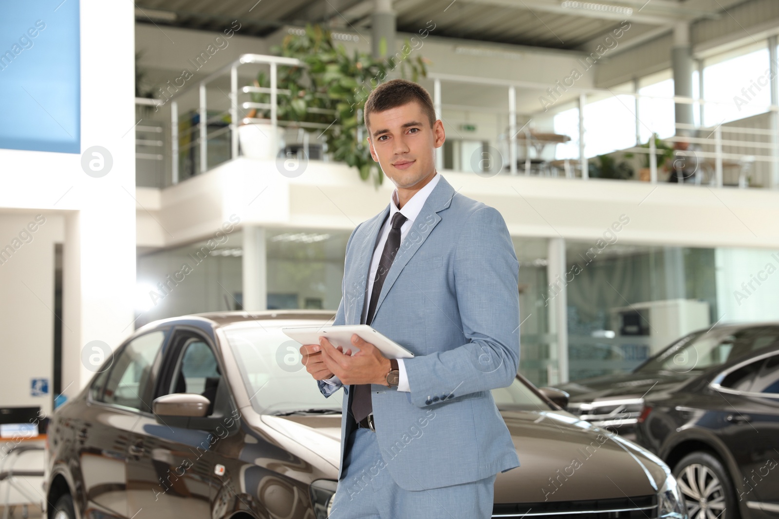 Photo of Young salesman with tablet in modern car dealership