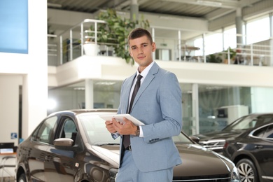 Young salesman with tablet in modern car dealership