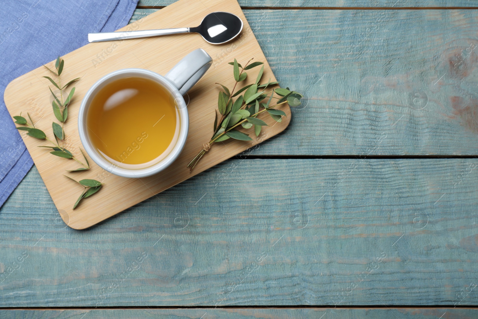 Photo of Cup of aromatic eucalyptus tea on light blue wooden table, top view. Space for text