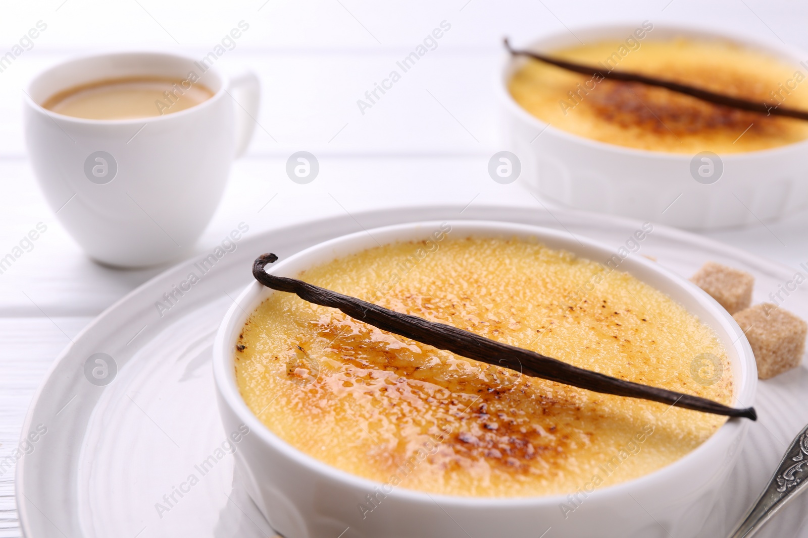 Photo of Delicious creme brulee in bowls, vanilla pods, sugar cubes and coffee on white wooden table, closeup