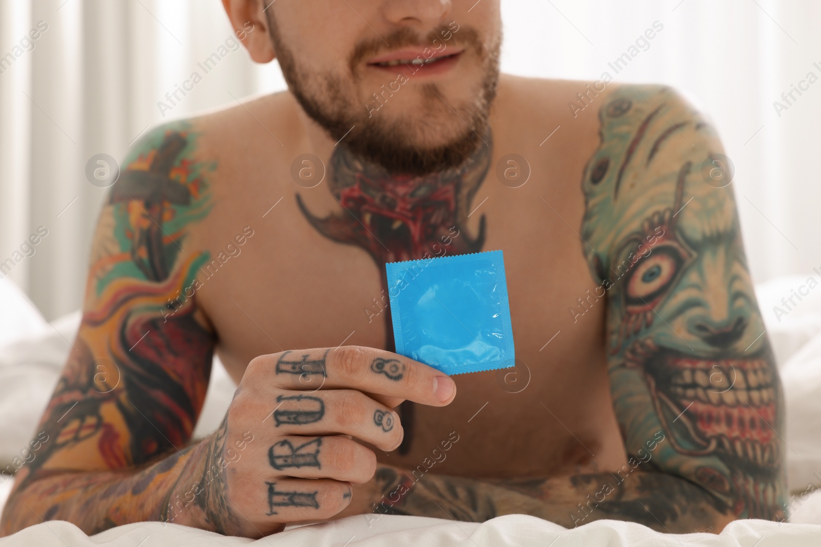 Photo of Man holding condom on bed at home, closeup