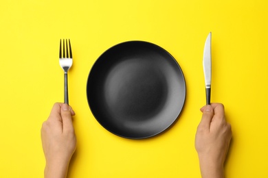 Woman with fork, knife and empty plate on color background, top view