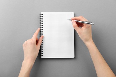 Photo of Woman writing in notebook on grey background, top view