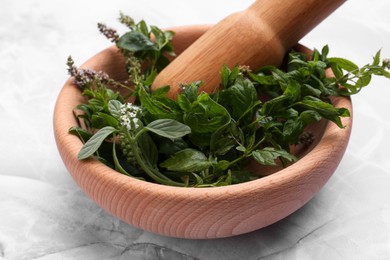 Mortar with pestle and mint leaves on light grey marble table, closeup