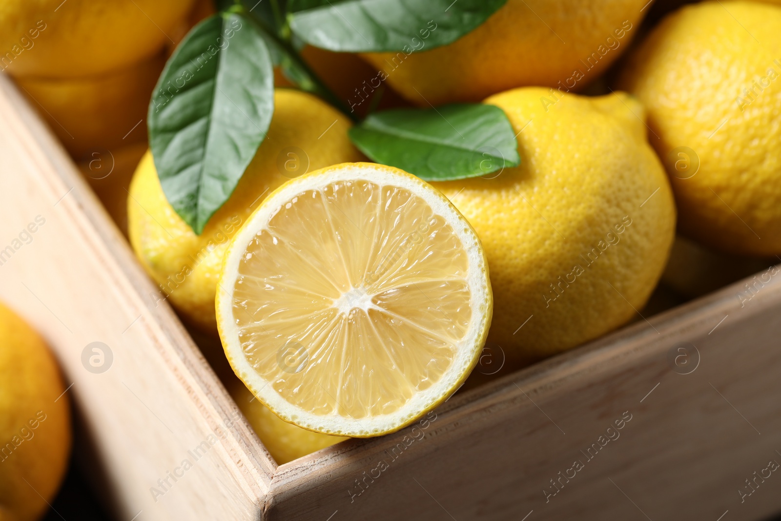 Photo of Fresh lemons and green leaves in wooden crate, closeup