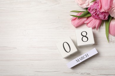 Photo of International Women's day - 8th of March. Block calendar and beautiful flowers on white wooden table, flat lay. Space for text