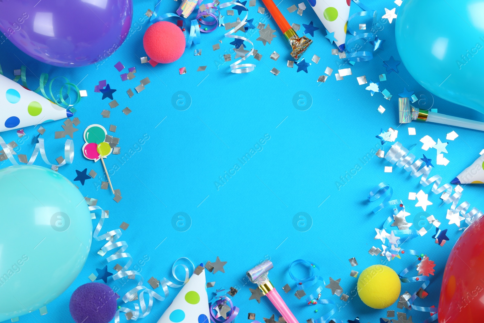 Photo of Frame of colorful serpentine streamers and other party accessories on light blue background, flat lay. Space for text