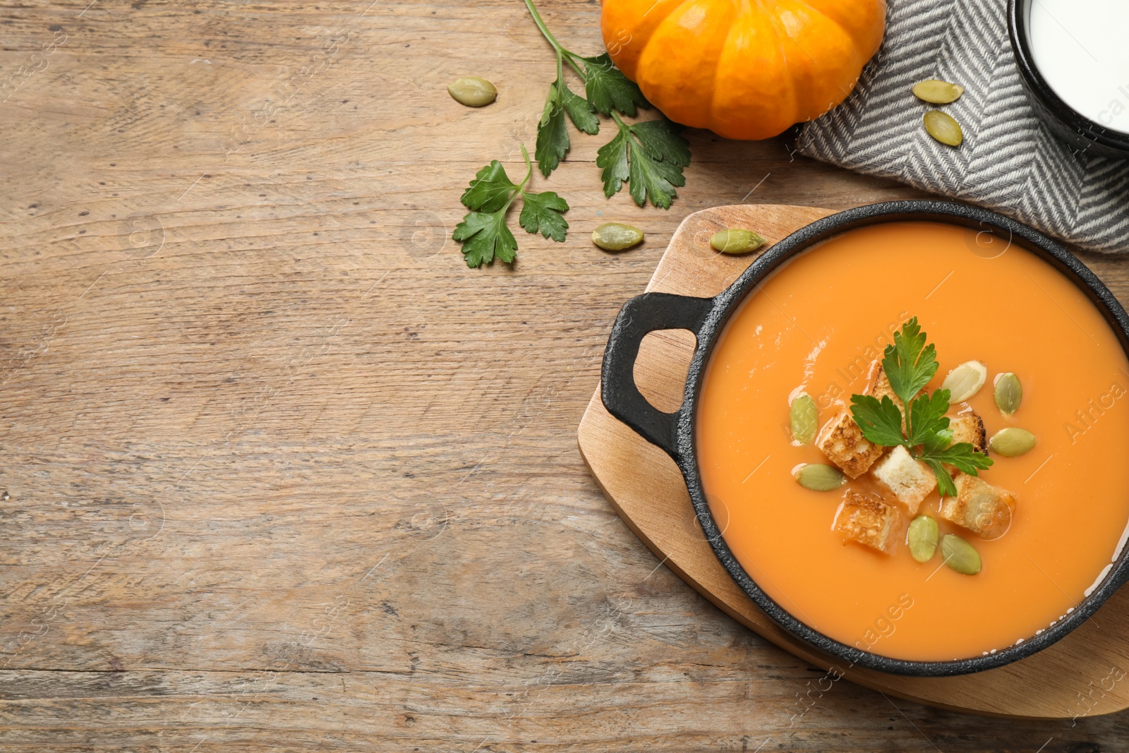 Photo of Tasty creamy pumpkin soup with croutons, seeds and parsley in bowl on wooden table, flat lay. Space for text