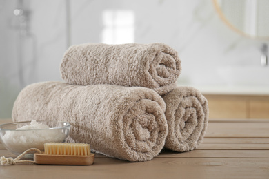Photo of Clean rolled towels, cosmetic salt and brush on wooden table in bathroom