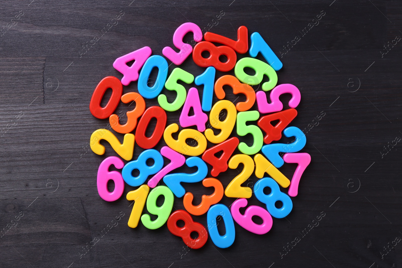 Photo of Colorful numbers on dark wooden school desk, top view