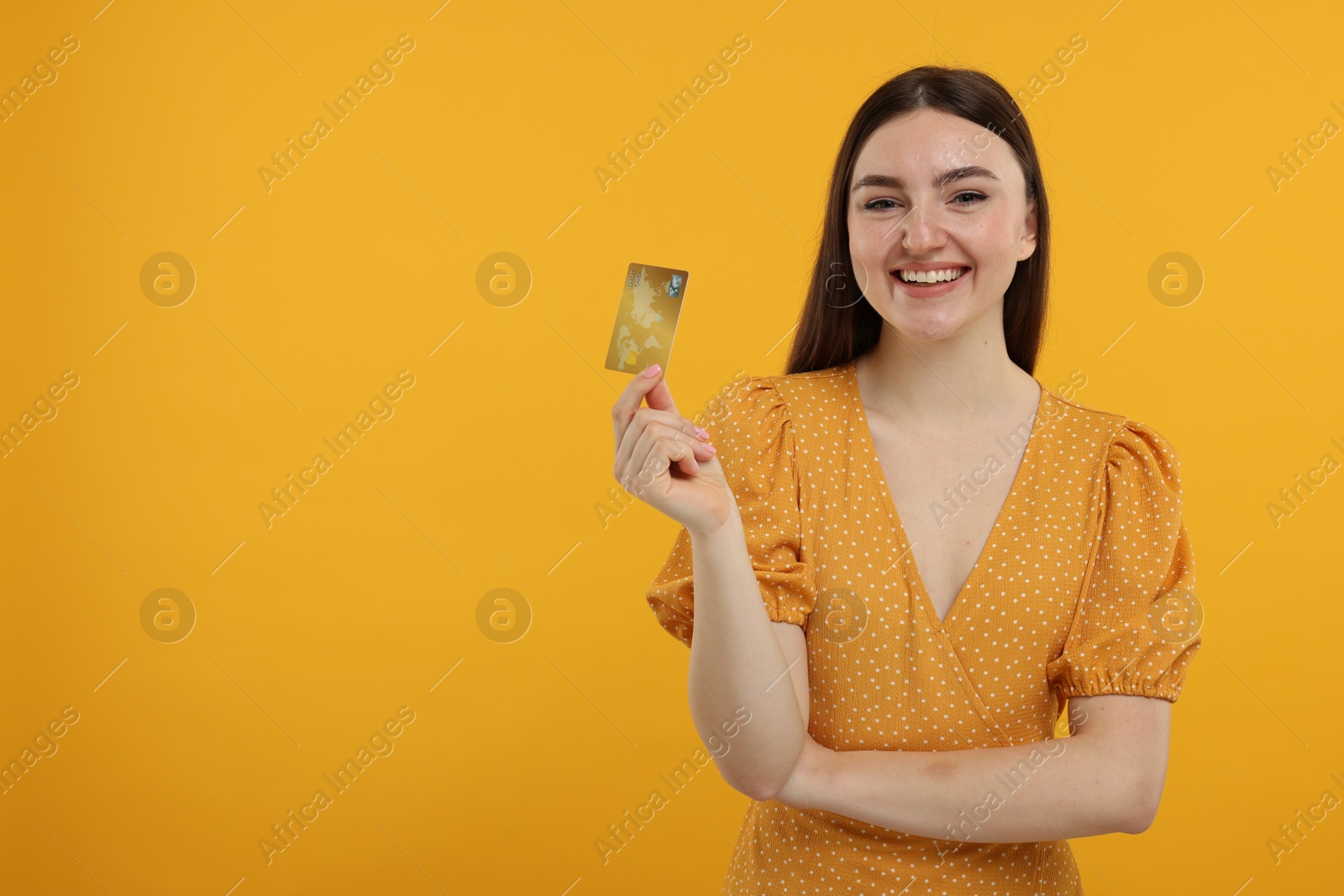 Photo of Happy woman with credit card on orange background, space for text