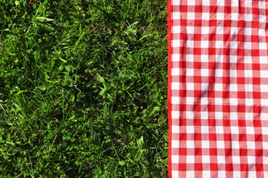 Photo of Checkered picnic tablecloth on fresh green grass, top view. Space for text