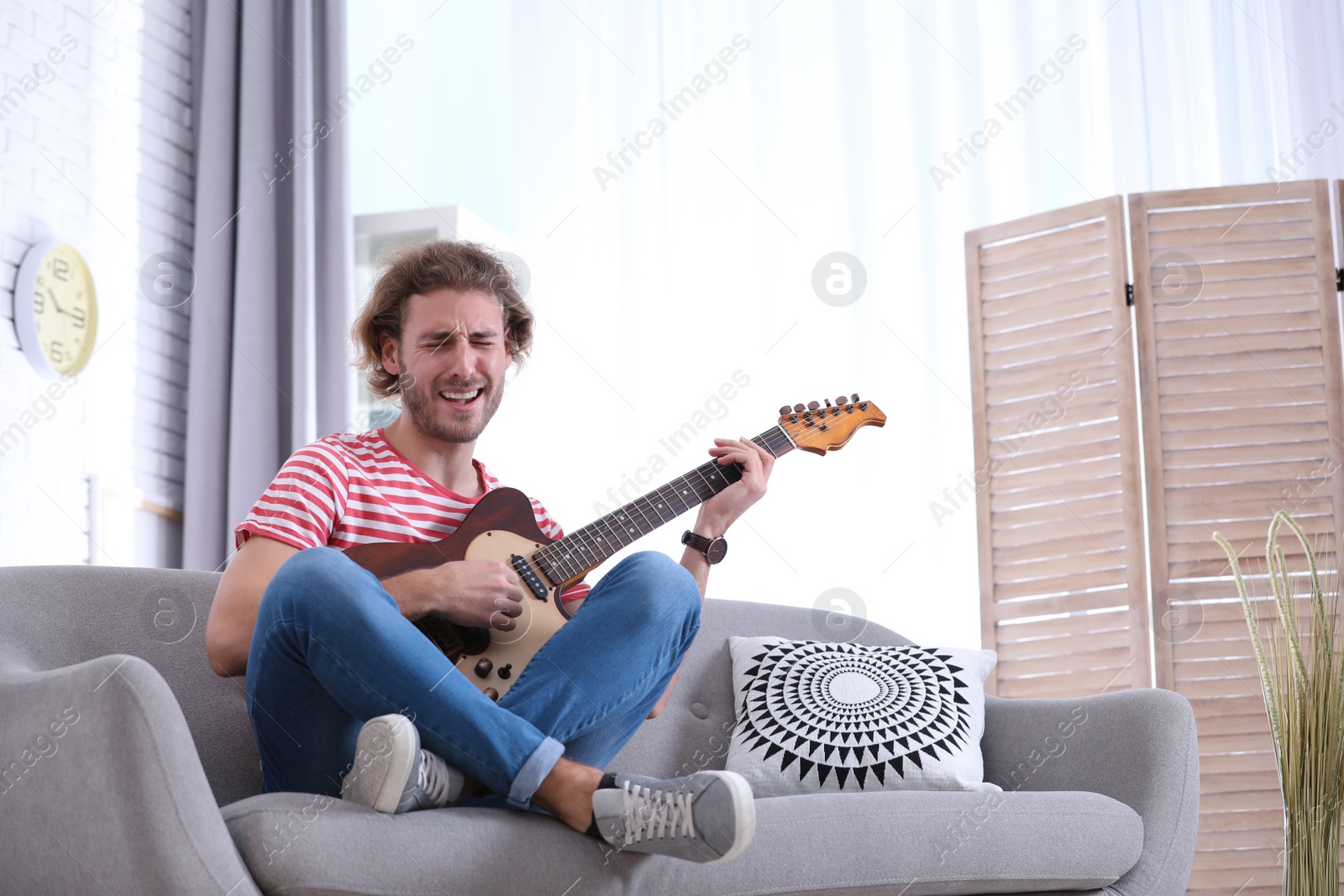 Photo of Young man playing electric guitar in living room. Space for text