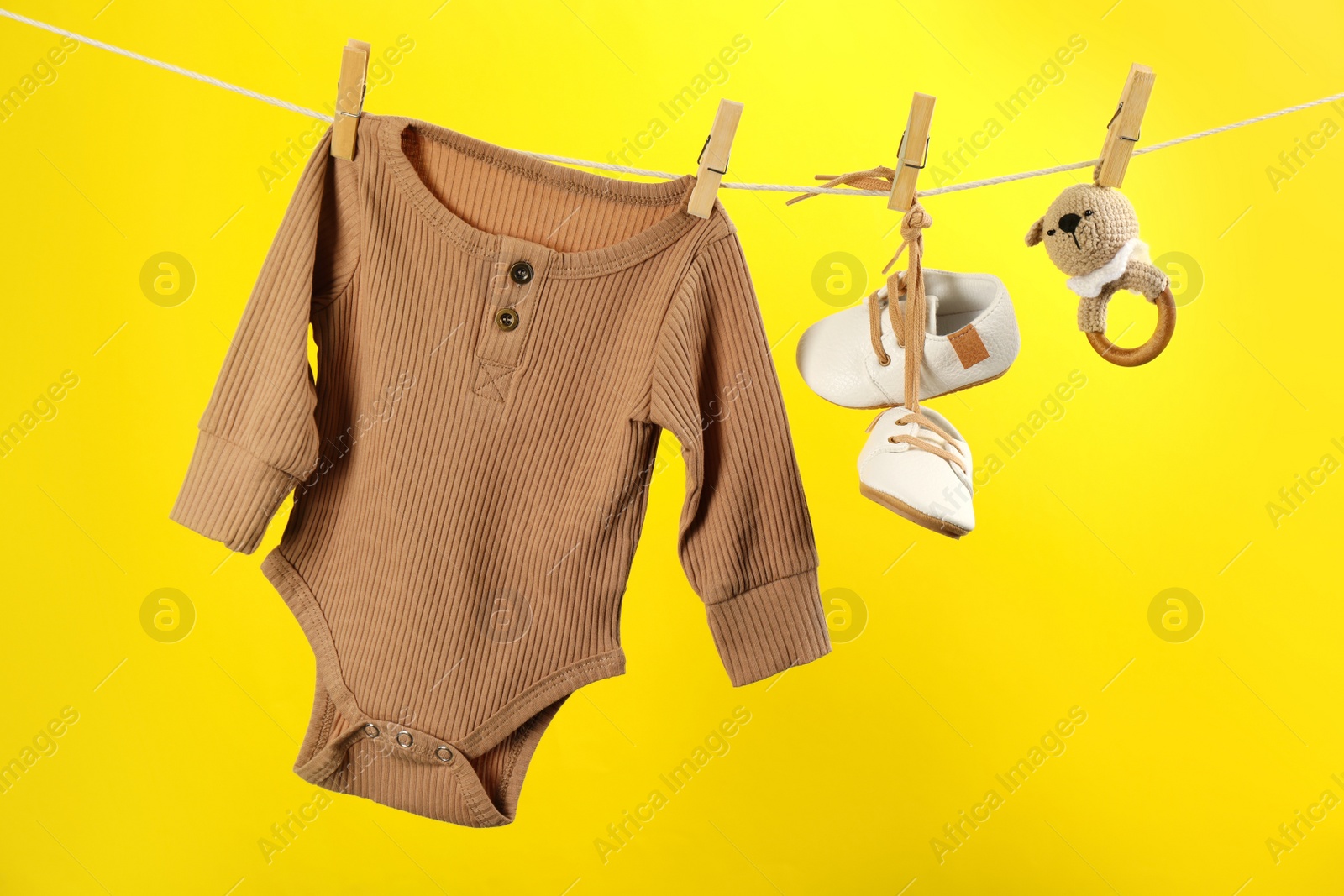Photo of Baby clothes and accessories hanging on washing line against yellow background