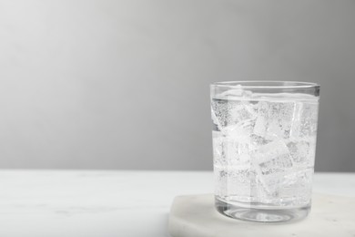 Photo of Glass of soda water with ice on white table. Space for text