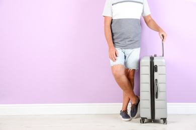 Photo of Senior man with suitcase near color wall. Space for text